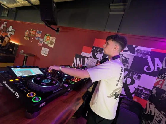Behind the decks in a bar, red wall covered in posters