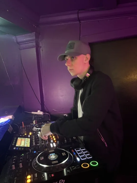 At the CDJs in a purple-lit room, looking out over the floor